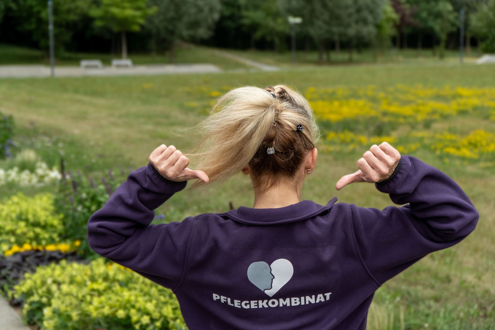 Mitarbeiterin des Pflegekombinats zeigt auf das Logo ihrer Arbeitskleidung